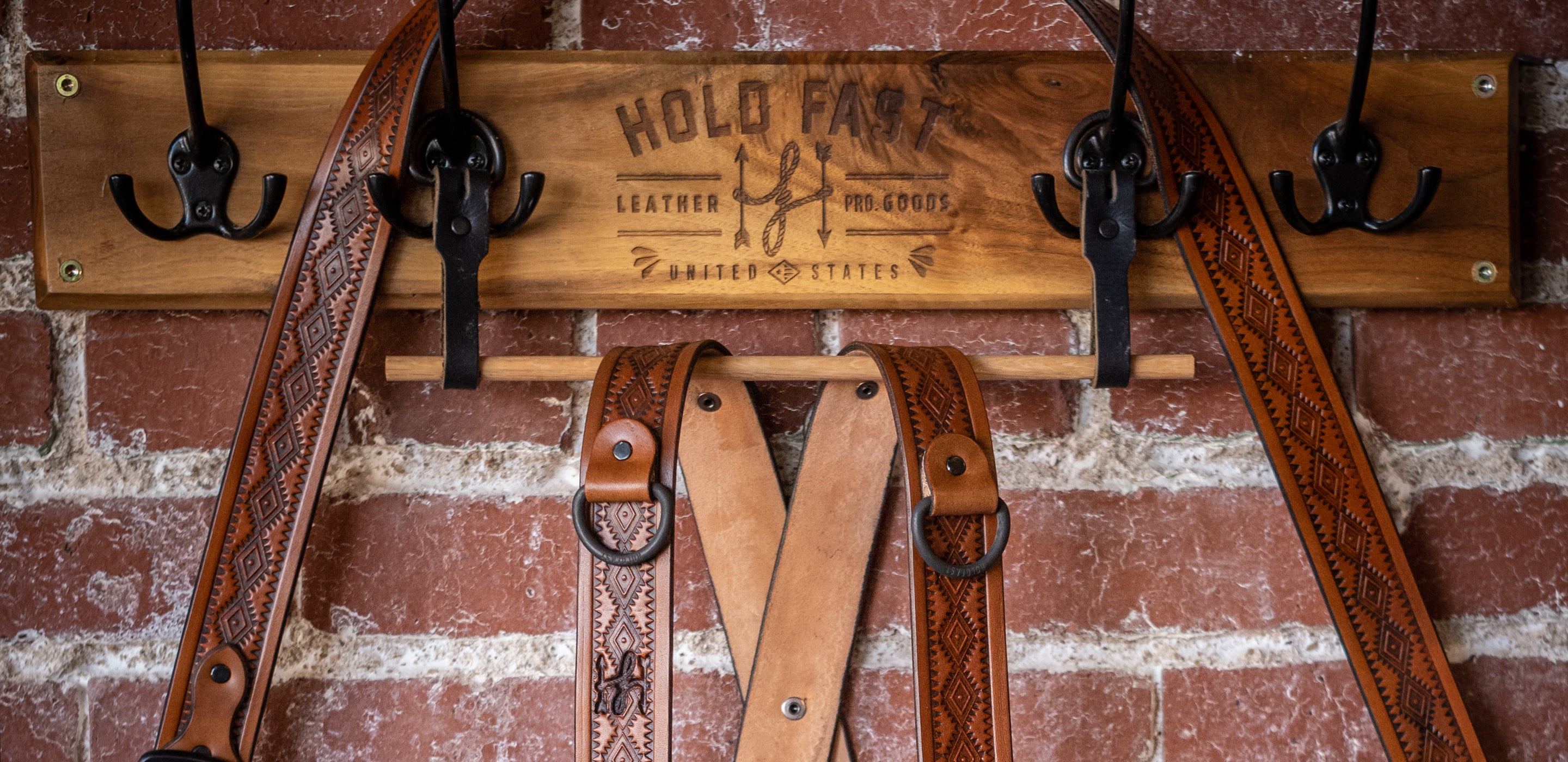 Wooden belt rack with leather belts and 'HoldFast branding against a brick wall.